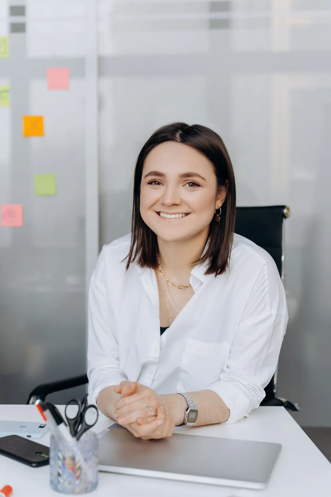 Smiling young woman in a white shirt sitting at her office desk